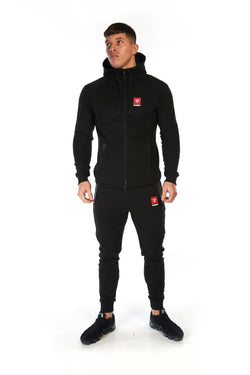 Man wearing black, slim fit tracksuit pants with red logo on the left thigh